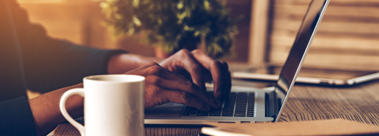 close up shot of a person on a laptop enjoying a cup of coffee.